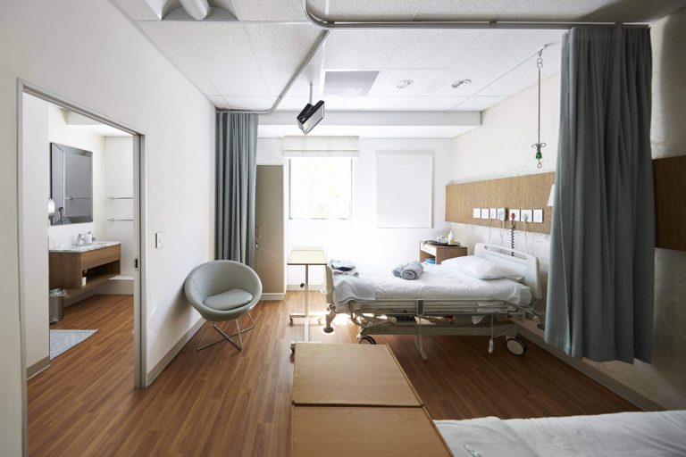 Moderne Krankenhauszimmer mit Bett, Stuhl und Zugang zu Bad und Fenster.