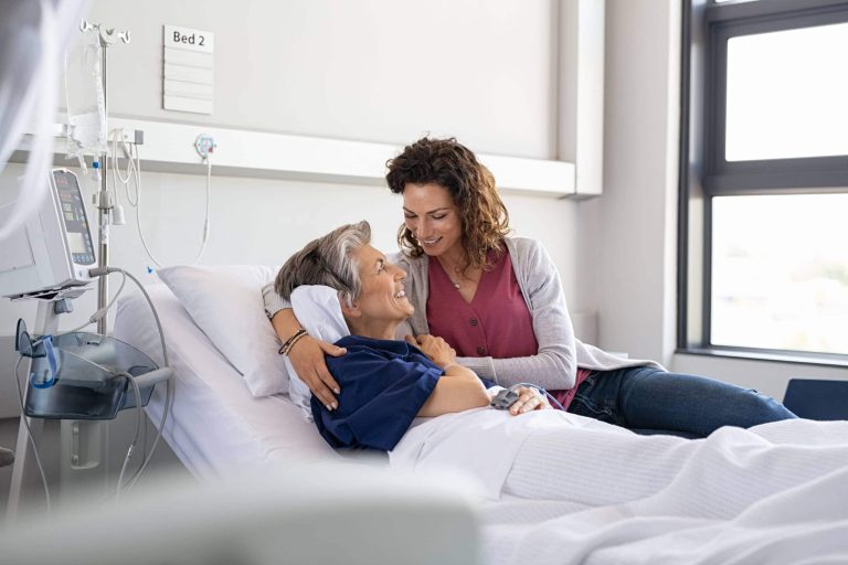 Pflegerin tröstet Patientin im Krankenhausbett, umgeben von medizinischer Ausrüstung.