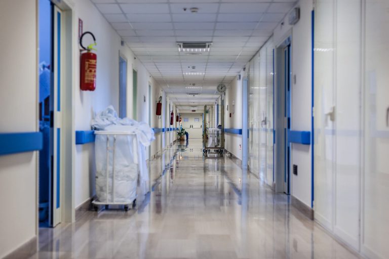 Leerer Krankenhausflur mit weißen Wänden, blauen Akzenten und medizinischen Wagen.