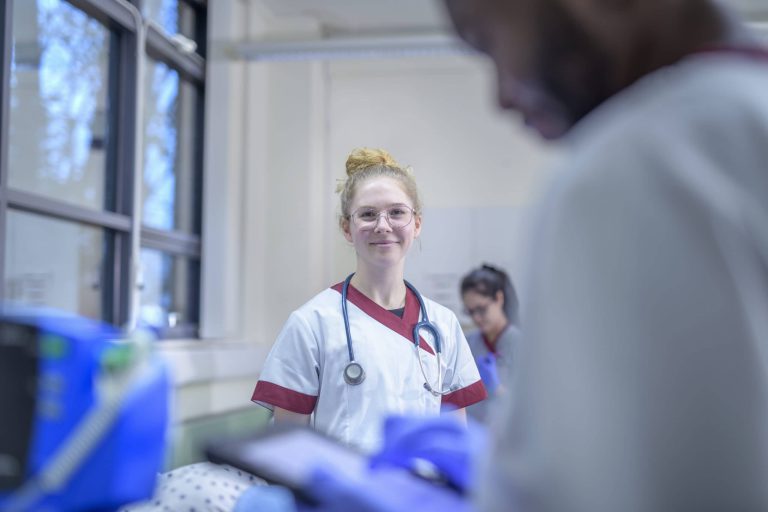 Lächelnde medizinische Fachkraft in einem Krankenhaus, umgeben von Kollegen und Patienten.